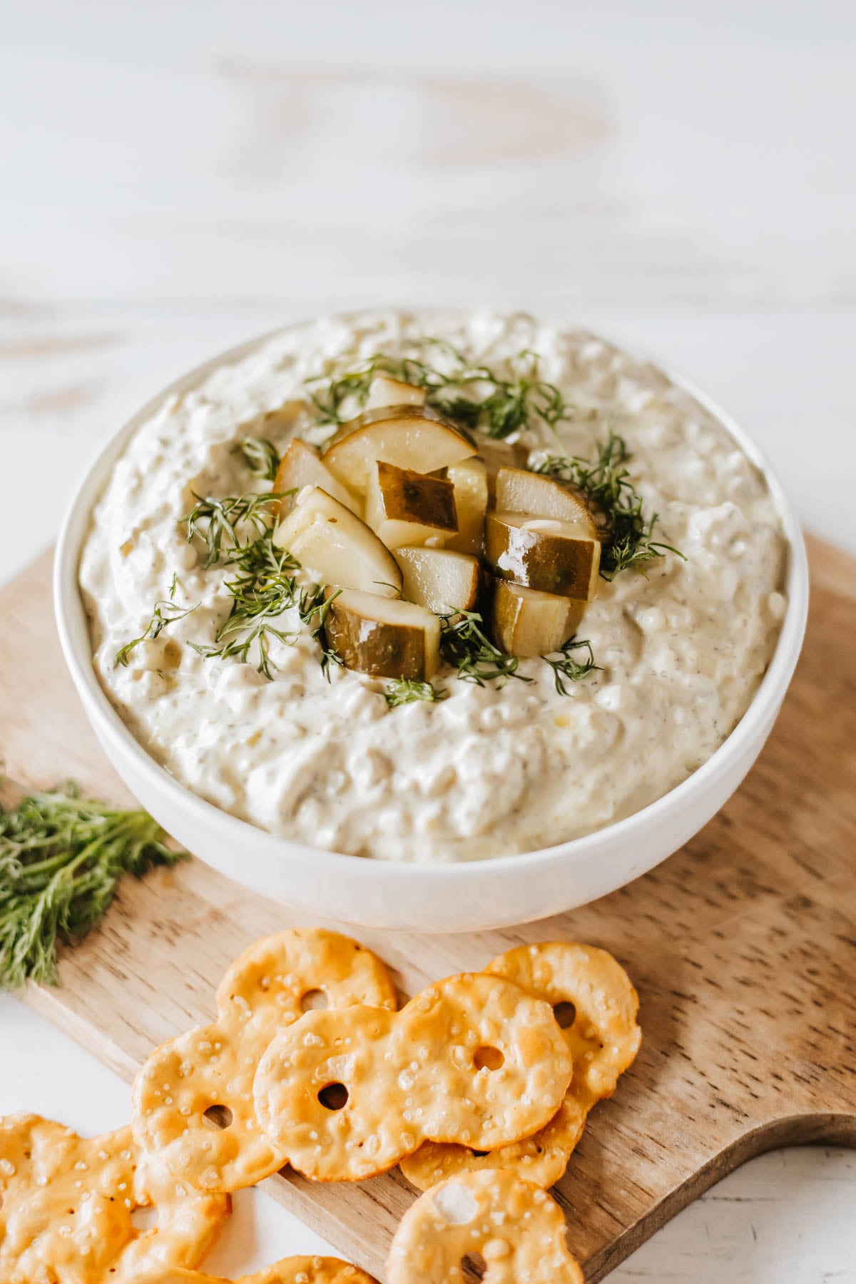Pickle Dip — Creamy, Tangy, and Completely Addictive 26 creamy pickle dip in a white bowl garnished with fresh dill and chopped dill pickles, surrounded by crackers and vegetables on a wooden board