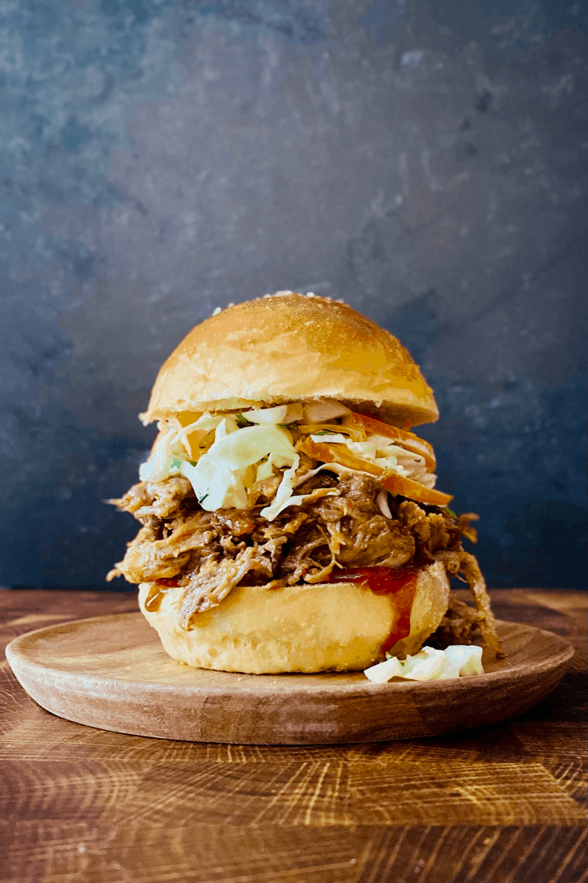 Pulled pork sandwiches piled high on toasted brioche buns with coleslaw and pickles on a rustic wooden board, golden summer light