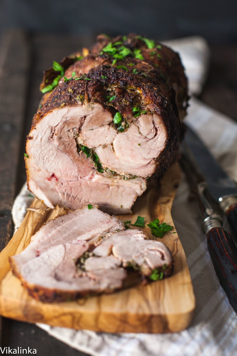 Pork shoulder coated in smoky dry rub spices on a cutting board surrounded by spice jars, garlic, and apple cider vinegar