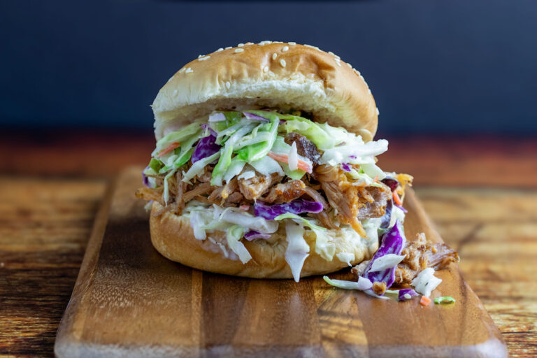 Close-up of a pulled pork sandwich cross-section showing juicy shredded pork, creamy coleslaw, and pickles on a toasted brioche bun