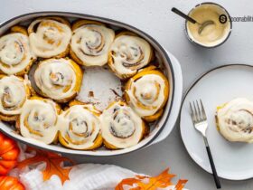Pumpkin Cinnamon Rolls with Cream Cheese Maple Icing — The Ultimate Overnight Fall Treat 34 Freshly baked pumpkin cinnamon rolls with cream cheese maple icing drizzled over the top in a white ceramic baking dish, shot from overhead on a rustic wooden table with cinnamon sticks and a small pumpkin as props