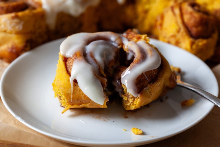 Pumpkin Cinnamon Rolls with Cream Cheese Maple Icing — The Ultimate Overnight Fall Treat 28 Close-up of a single pumpkin cinnamon roll on a white plate with cream cheese maple icing dripping down the sides, garnished with a dusting of cinnamon and a drizzle of maple syrup, morning light streaming in from the side