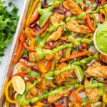 Sheet Pan Chicken Fajitas beautifully plated on a large wooden board with warm tortillas, sliced avocado, lime wedges, fresh cilantro, and colorful roasted peppers