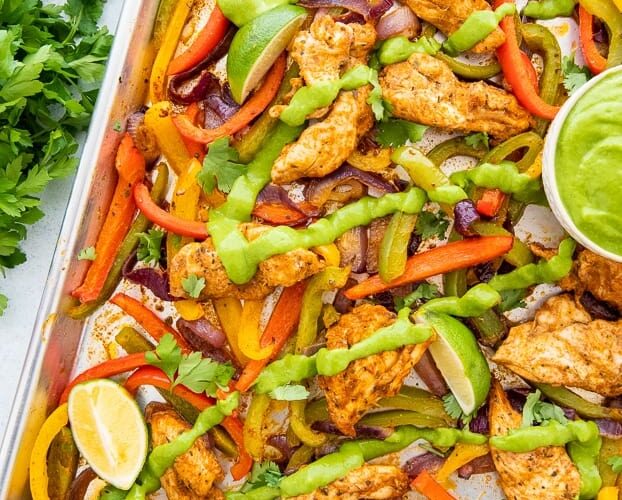 Sheet Pan Chicken Fajitas beautifully plated on a large wooden board with warm tortillas, sliced avocado, lime wedges, fresh cilantro, and colorful roasted peppers