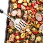 Sheet pan sausage and peppers with roasted potatoes and onions on a large baking sheet, golden and caramelized, garnished with fresh parsley