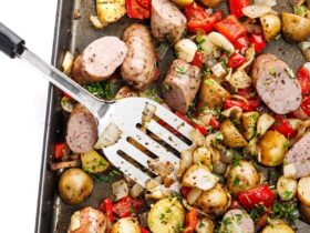 Sheet pan sausage and peppers with roasted potatoes and onions on a large baking sheet, golden and caramelized, garnished with fresh parsley