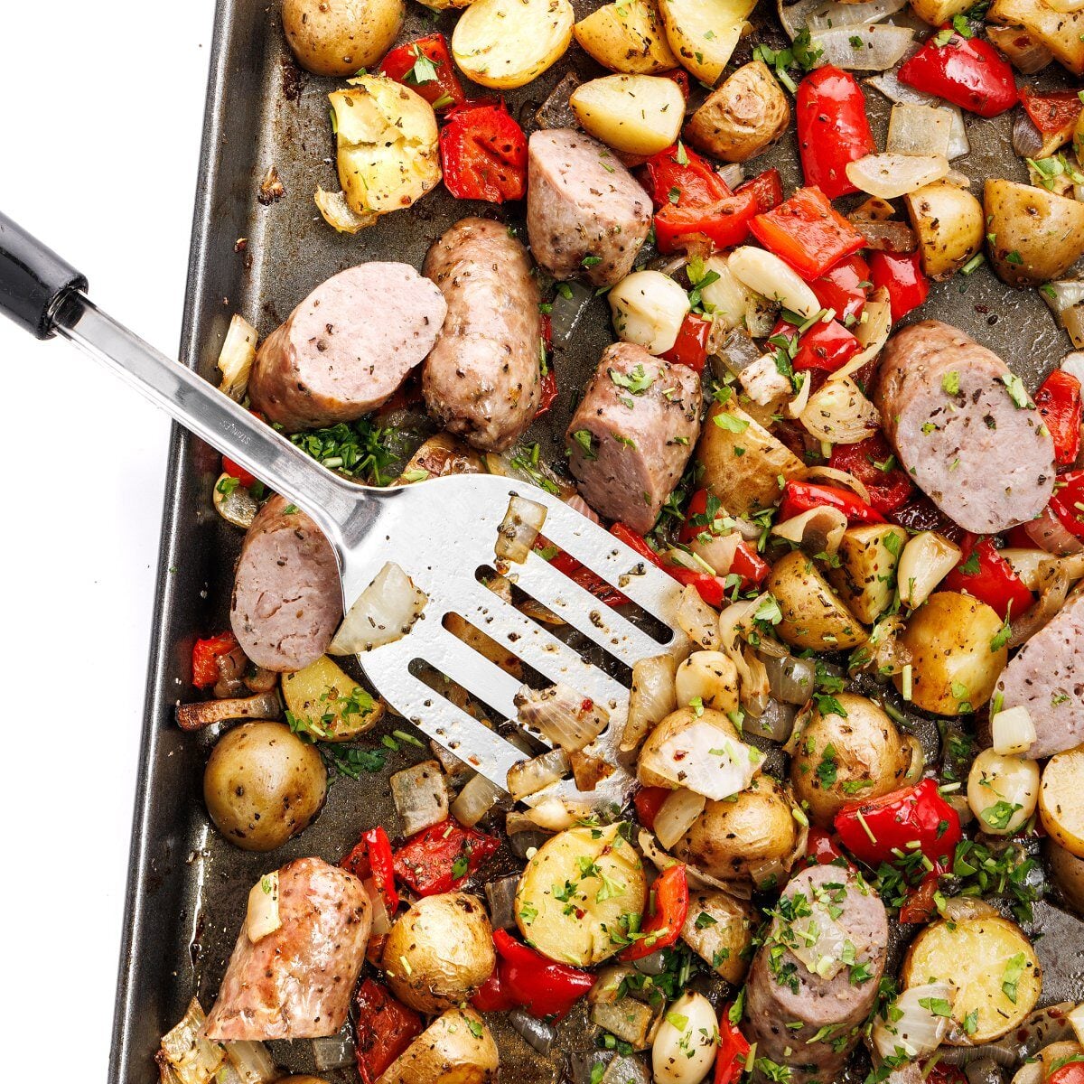 Sheet pan sausage and peppers with roasted potatoes and onions on a large baking sheet, golden and caramelized, garnished with fresh parsley