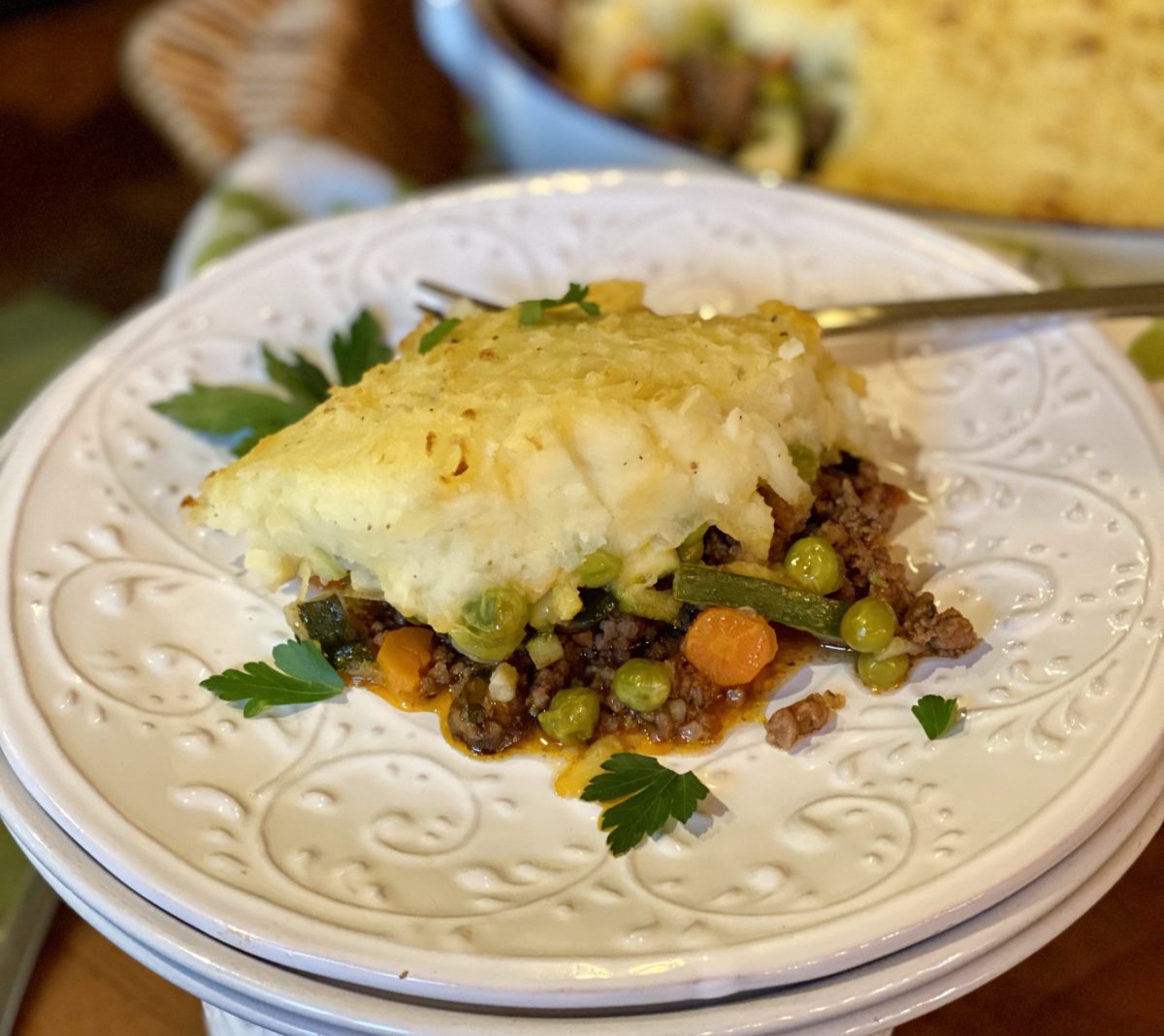 Overhead flat lay of Shepherd's Pie ingredients including ground lamb, diced carrots, celery, peas, rosemary, thyme, and russet potatoes arranged on a linen surface