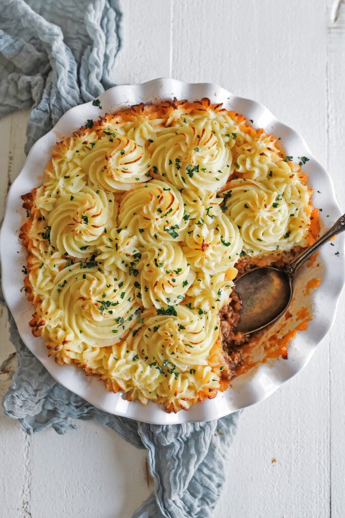 Close-up of a serving of Shepherd's Pie on a white plate showing the golden mashed potato crust and rich lamb and vegetable filling underneath