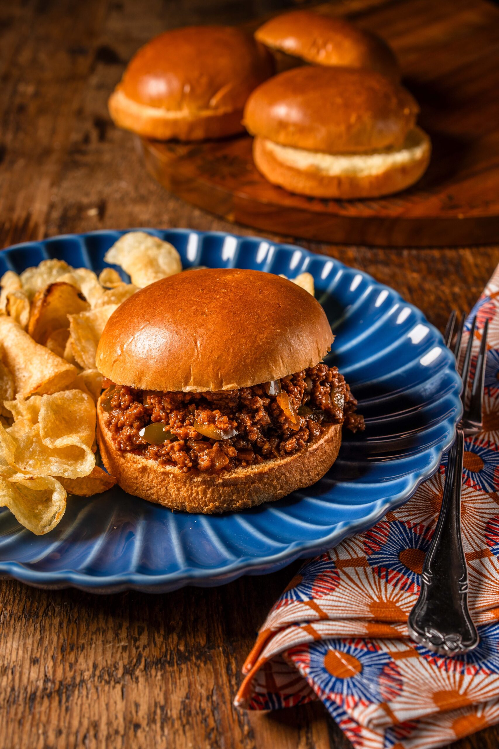 Overhead shot of Sloppy Joe ingredients laid out on a white surface — ground beef, diced onion, bell pepper, tomato paste, Worcestershire sauce, spices, and buns