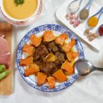 Slow cooker beef stew served in a rustic white bowl with fork-tender beef chunks, golden carrots, soft potatoes, and glistening herb gravy, garnished with fresh thyme on a wooden table