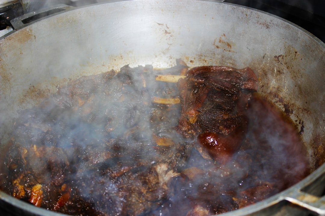 Close-up of a ladle lifting slow cooker beef stew from the pot, showing glossy rich herb gravy, chunks of tender beef, and colorful vegetables with steam rising