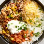 Slow cooker chicken burrito bowls served in a white bowl with shredded chicken, rice, black beans, corn, and fresh toppings including avocado, sour cream, and cilantro