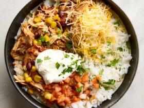 Slow cooker chicken burrito bowls served in a white bowl with shredded chicken, rice, black beans, corn, and fresh toppings including avocado, sour cream, and cilantro