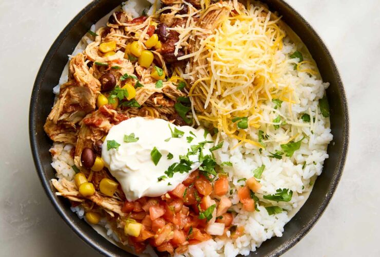 Slow cooker chicken burrito bowls served in a white bowl with shredded chicken, rice, black beans, corn, and fresh toppings including avocado, sour cream, and cilantro