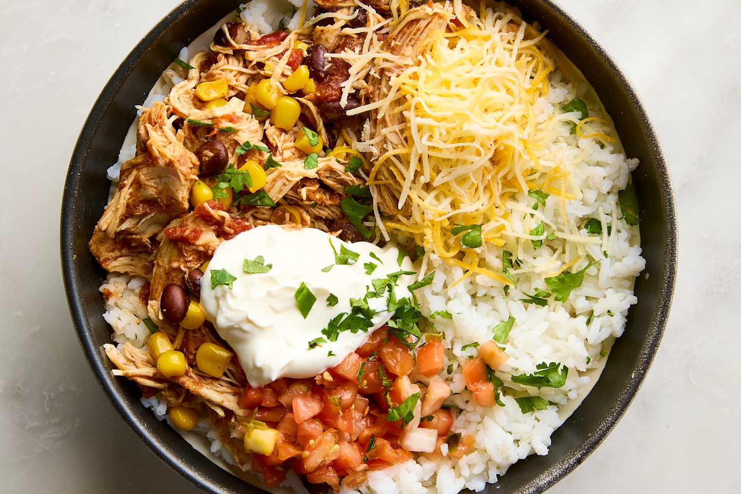 Slow cooker chicken burrito bowls served in a white bowl with shredded chicken, rice, black beans, corn, and fresh toppings including avocado, sour cream, and cilantro