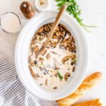 Slow cooker chicken wild rice soup served in a rustic white bowl, garnished with fresh thyme, steam rising, on a wooden table with a cozy linen napkin