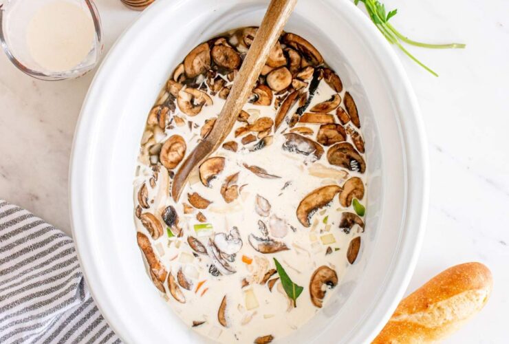 Slow cooker chicken wild rice soup served in a rustic white bowl, garnished with fresh thyme, steam rising, on a wooden table with a cozy linen napkin