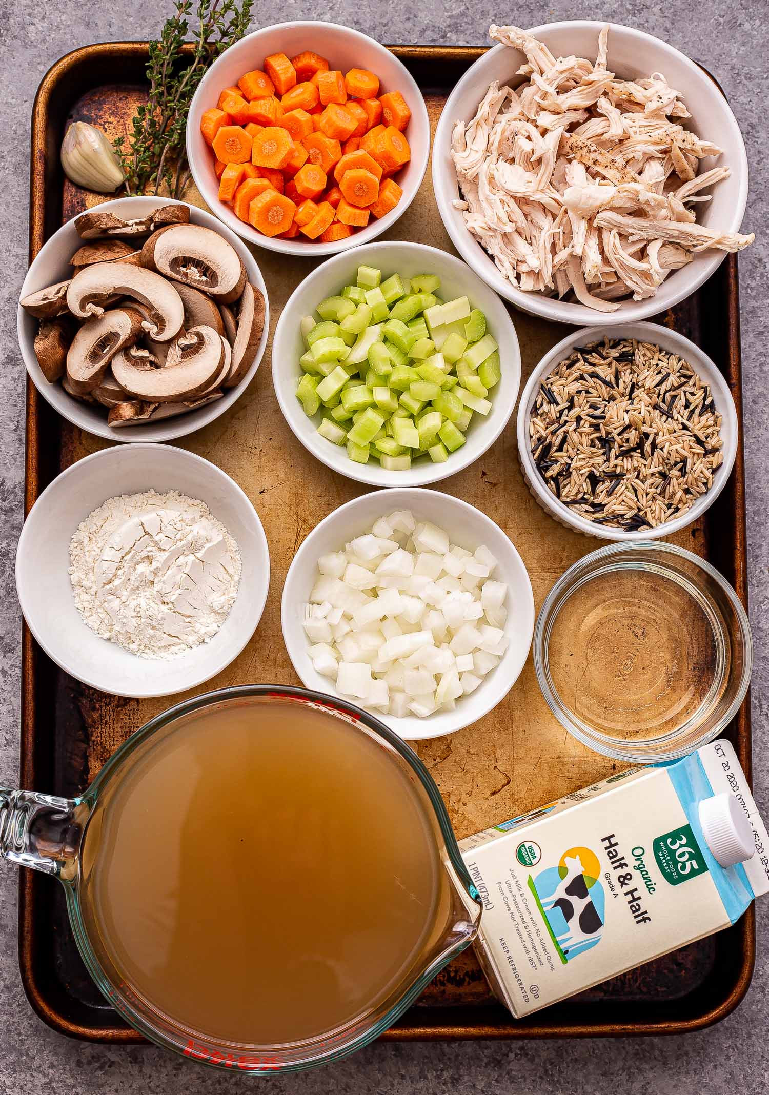 Slow Cooker Chicken Wild Rice Soup — Creamy, Hearty & Deeply Nourishing 27 Overhead flat-lay of slow cooker chicken wild rice soup ingredients — wild rice, chicken thighs, carrots, celery, onion, garlic, thyme, broth, and cream arranged on a light marble surface