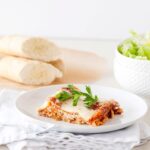 Slow cooker lasagna served on a white plate with fresh basil and a side salad, beautifully plated and golden cheesy on top