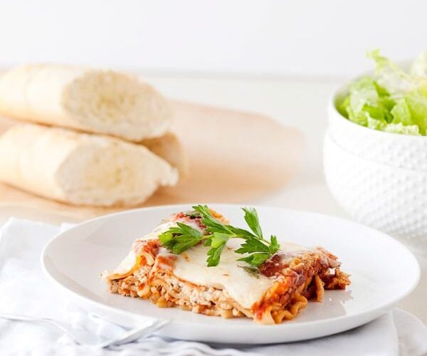 Slow cooker lasagna served on a white plate with fresh basil and a side salad, beautifully plated and golden cheesy on top