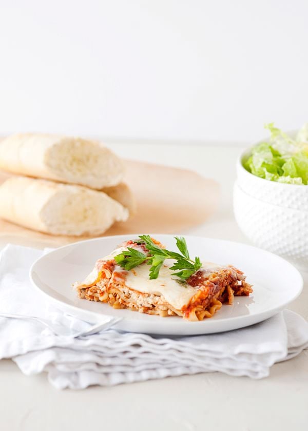 Slow cooker lasagna served on a white plate with fresh basil and a side salad, beautifully plated and golden cheesy on top