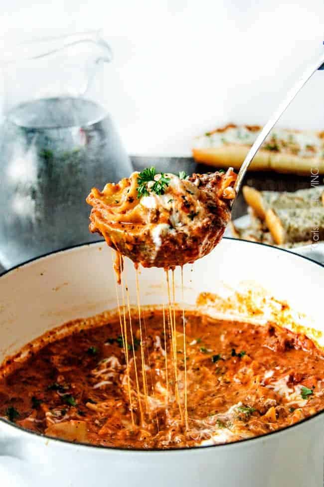 Overhead flat-lay of slow cooker lasagna ingredients including ricotta, marinara sauce, no-boil noodles, ground beef, mozzarella, and fresh herbs arranged on a wooden board
