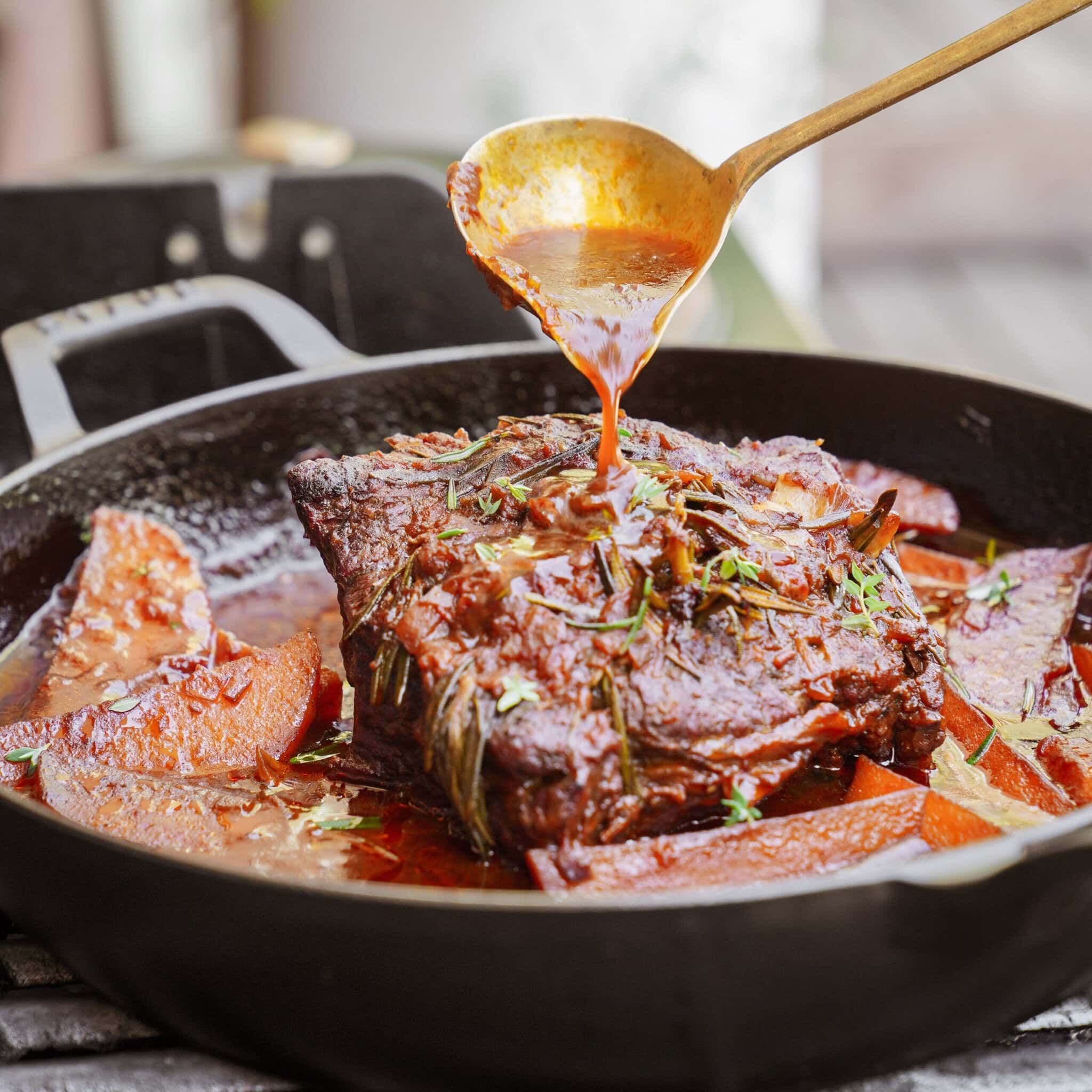 Slow Cooker Pot Roast — Classic Chuck Roast with Root Vegetables and Savory Gravy 27 Chuck roast being seared in a cast iron skillet with garlic, herbs, and root vegetables arranged alongside on a wooden cutting board