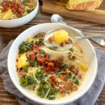 A steaming bowl of Slow Cooker Zuppa Toscana with creamy broth, Italian sausage slices, golden potato rounds, and vibrant green kale, garnished with red pepper flakes and crusty bread on the side
