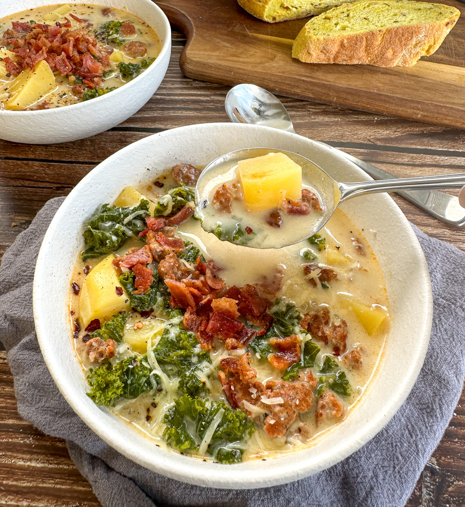 A steaming bowl of Slow Cooker Zuppa Toscana with creamy broth, Italian sausage slices, golden potato rounds, and vibrant green kale, garnished with red pepper flakes and crusty bread on the side
