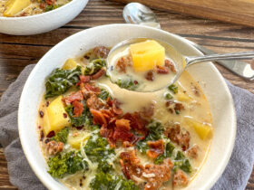 A steaming bowl of Slow Cooker Zuppa Toscana with creamy broth, Italian sausage slices, golden potato rounds, and vibrant green kale, garnished with red pepper flakes and crusty bread on the side