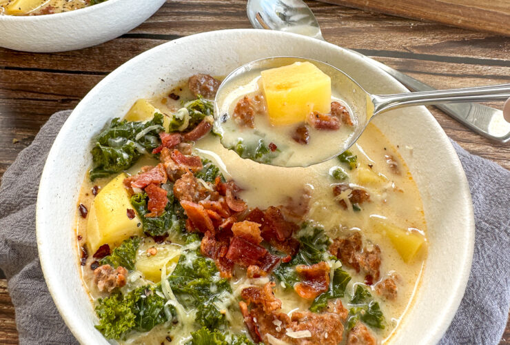 A steaming bowl of Slow Cooker Zuppa Toscana with creamy broth, Italian sausage slices, golden potato rounds, and vibrant green kale, garnished with red pepper flakes and crusty bread on the side