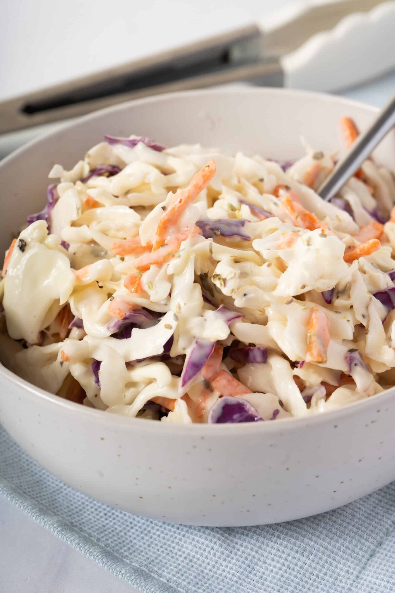 Southern Coleslaw served in a large white bowl with a tangy creamy dressing, garnished with fresh parsley, photographed on a rustic wooden picnic table with BBQ sides in the background
