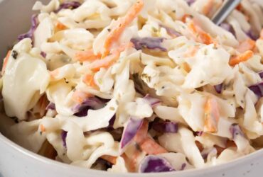 Southern Coleslaw served in a large white bowl with a tangy creamy dressing, garnished with fresh parsley, photographed on a rustic wooden picnic table with BBQ sides in the background