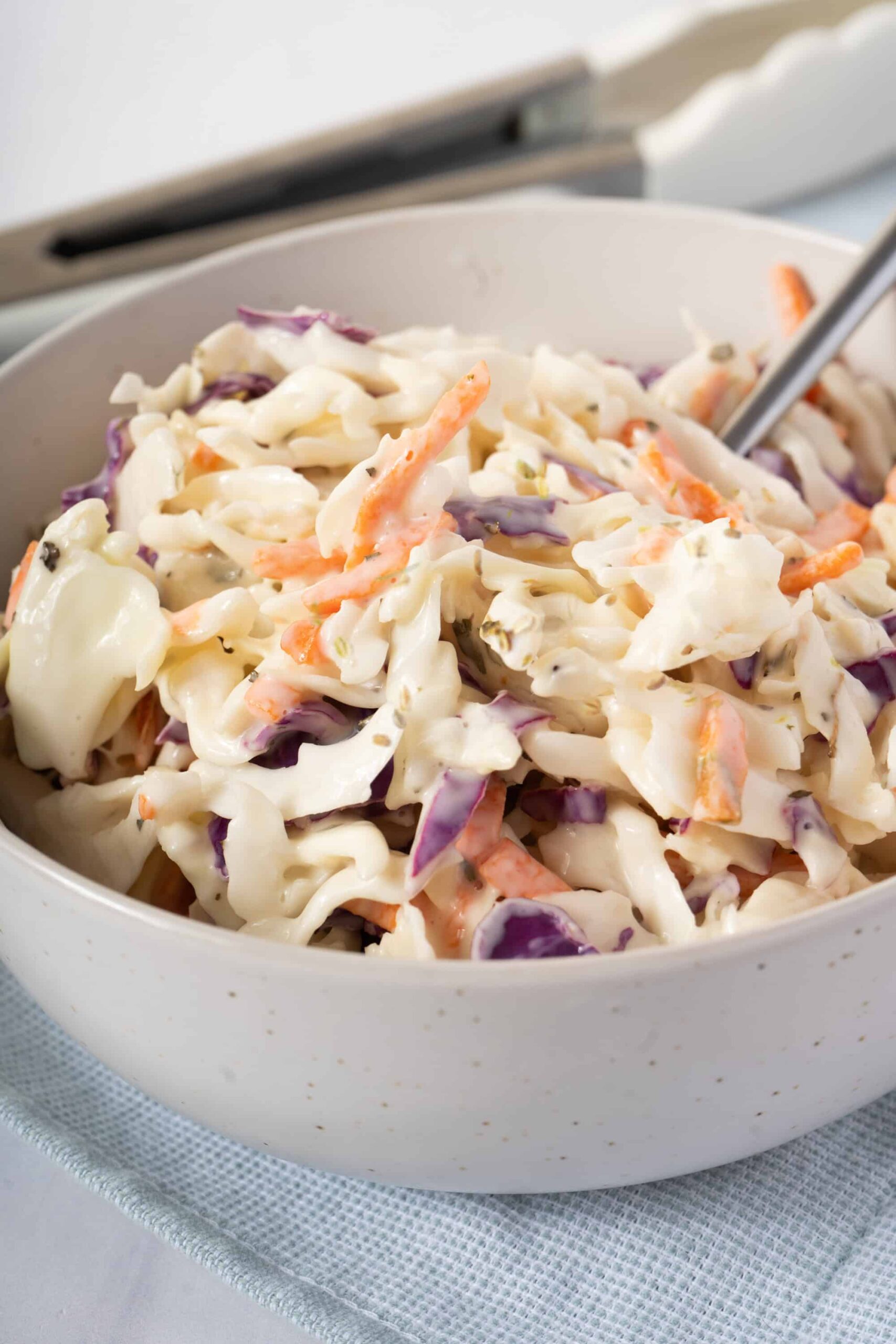 Southern Coleslaw served in a large white bowl with a tangy creamy dressing, garnished with fresh parsley, photographed on a rustic wooden picnic table with BBQ sides in the background