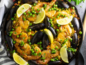 Overhead shot of a vibrant Spanish Paella in a wide pan, golden saffron rice topped with shrimp, mussels, chicken, roasted red peppers, and fresh lemon wedges, photographed on a rustic wooden table
