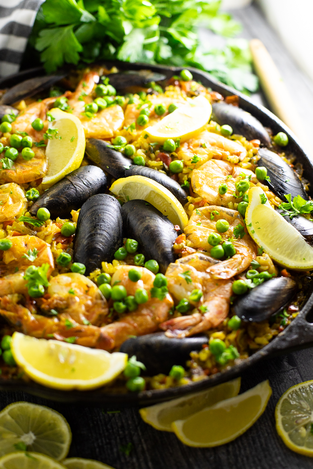 Close-up of Spanish Paella in the pan, showing golden saffron rice with a beautifully charred socarrat bottom, whole shrimp, fresh lemon wedges, and a sprinkle of chopped parsley