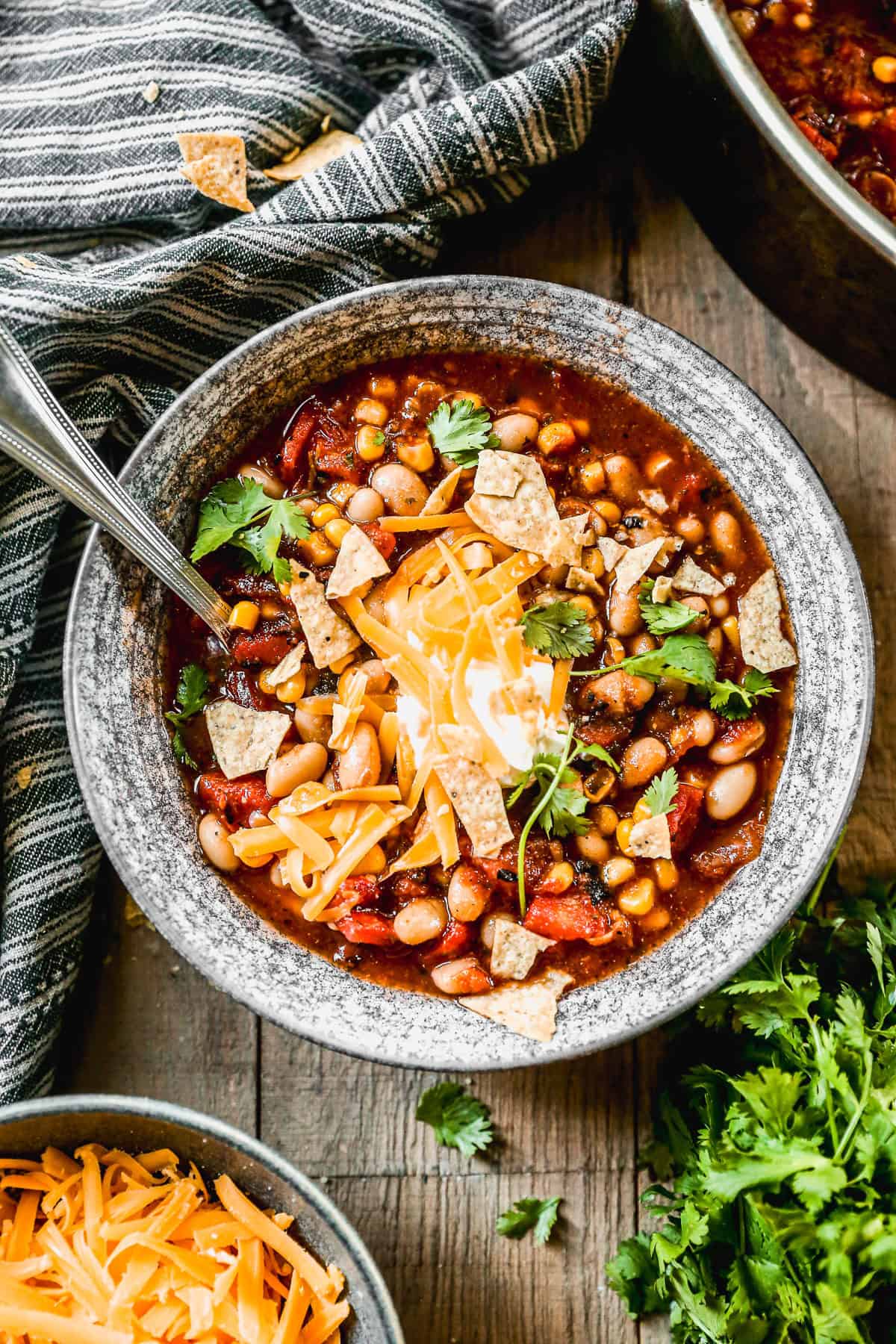 A rustic bowl of taco soup topped with shredded cheddar, sour cream, jalapeño slices, crushed tortilla chips, and fresh cilantro on a wooden table