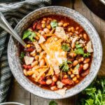 A steaming bowl of taco soup topped with shredded cheese, sour cream, sliced jalapeños, and fresh cilantro, photographed on a rustic wooden table with warm golden light