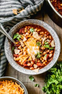 A steaming bowl of taco soup topped with shredded cheese, sour cream, sliced jalapeños, and fresh cilantro, photographed on a rustic wooden table with warm golden light