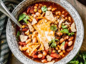 A steaming bowl of taco soup topped with shredded cheese, sour cream, sliced jalapeños, and fresh cilantro, photographed on a rustic wooden table with warm golden light