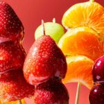 Tanghulu Candied Fruit skewers with strawberries and grapes, glistening sugar shell, arranged on a marble surface with a snowy white backdrop