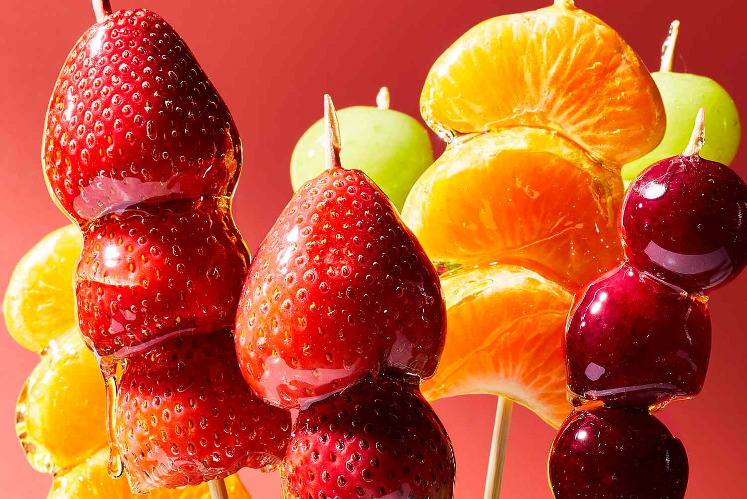 Tanghulu Candied Fruit skewers with strawberries and grapes, glistening sugar shell, arranged on a marble surface with a snowy white backdrop