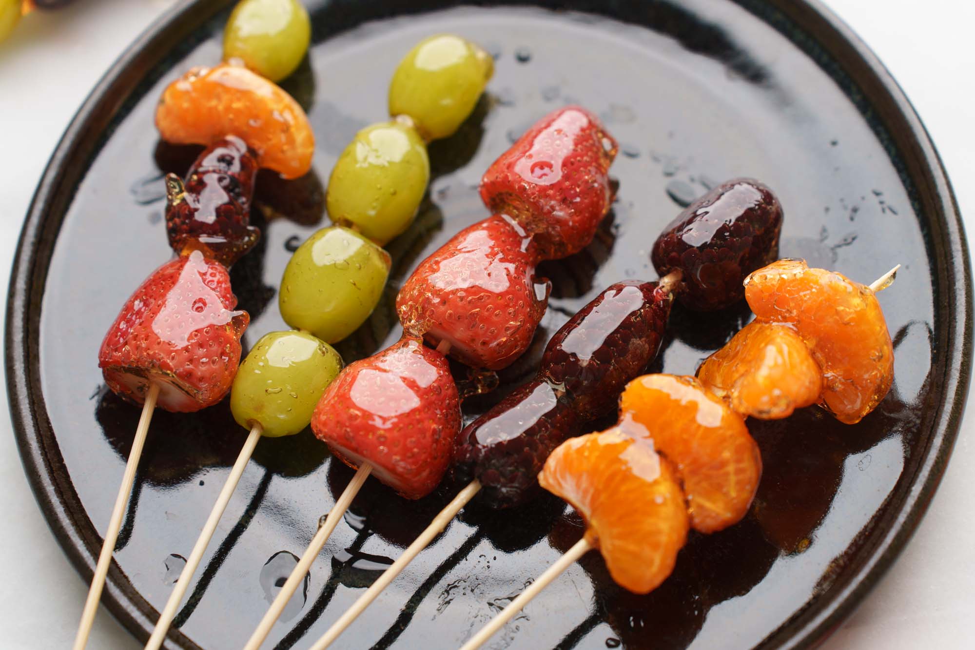Step-by-step process shots of making Tanghulu — sugar syrup bubbling in pot, fruit being dipped, sugar shell hardening on skewers laid on parchment paper