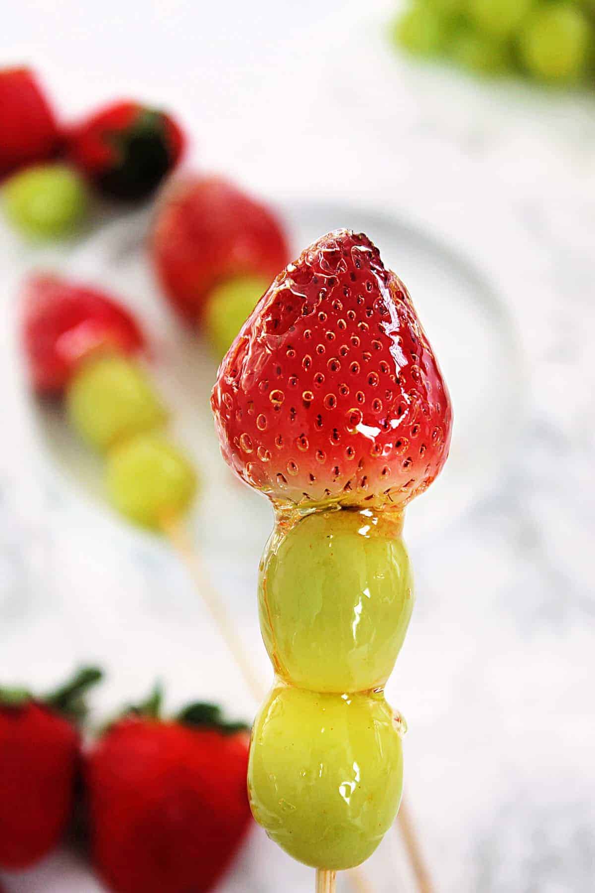 Close-up of Tanghulu Candied Fruit skewer with strawberries, the glassy sugar shell reflecting light, held up against a soft bokeh background