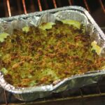 Golden tater tot casserole fresh from the oven in a white baking dish, topped with melted cheddar cheese and crispy tots, garnished with fresh parsley on a rustic wooden table