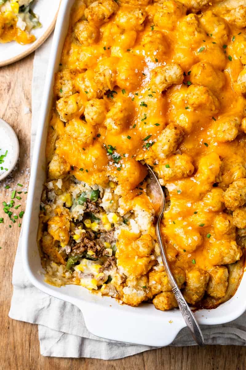 Tater Tot Casserole — The Ultimate Crispy, Cheesy Ground Beef Comfort Bake 28 Close-up serving of tater tot casserole on a white plate showing the crispy golden tot layer, melted cheddar, and savory beef filling with steam rising, fork resting on the side