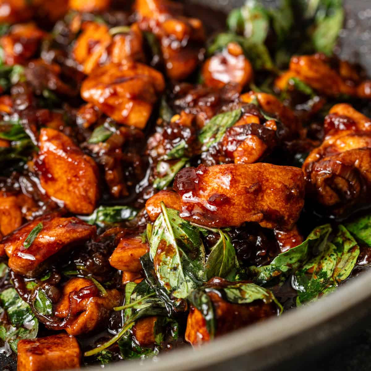Overhead flat lay of Thai Basil Chicken ingredients — ground chicken, garlic cloves, bird's eye chilies, fish sauce, oyster sauce, fresh basil, and soy sauce arranged on a white marble surface