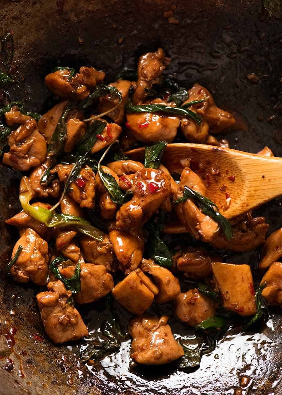 Close-up of Thai Basil Chicken in a wok with a crispy fried egg on top, fresh basil leaves scattered around, sauce glistening over the ground chicken, shot with shallow depth of field