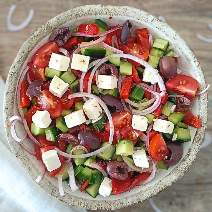 Close-up of a fork breaking into a creamy slab of feta cheese atop a Traditional Greek Salad with glistening olive oil and vibrant tomato wedges visible in the background